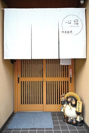A traditional Japanese entrance with a sliding door, a mat, and a decorative figure.