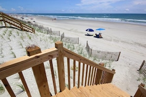 Een houten trap die leidt naar een zandstrand, met een houten hek en een blauwe parasol.