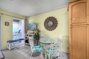 A dining area with a glass table, white chairs, and a bench. - Oceanfront 1BR • Top-Floor Balcony Views • Cherry Grove • Sea Cabin 304-A (North Myrtle Beach)