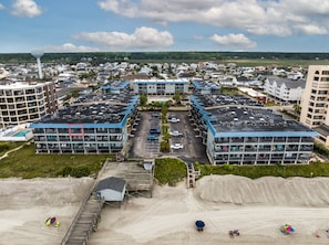 Un hôtel à plusieurs étages doté d’un parking, d’une plage avec du sable et des parasols, et offrant une vue lointaine sur un quartier résidentiel.