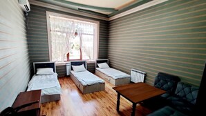 A compact room with three single beds, a wooden table, a sofa, and a window with curtains. - Ozbek Hotel (Andijan)