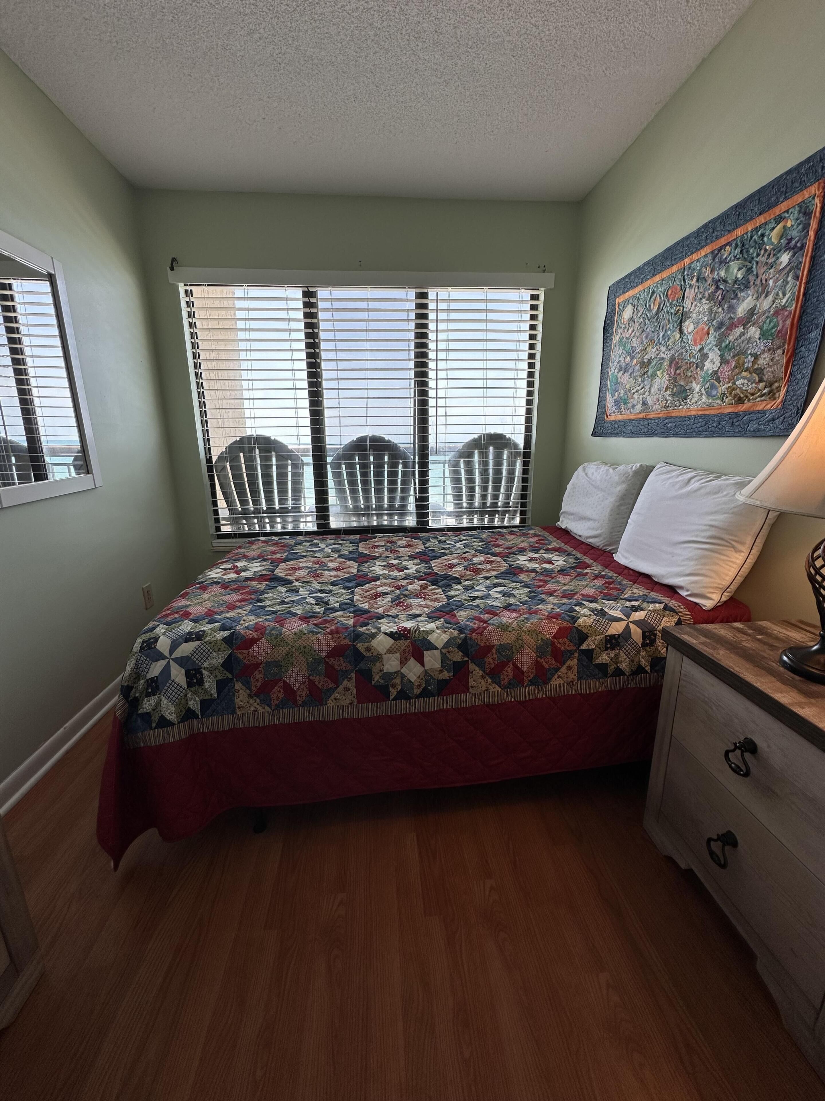 A bedroom with a bed, a window with blinds, a chair, a nightstand, and a wall painting.