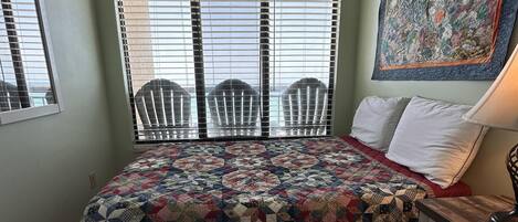 A bedroom with a bed, a window with blinds, a chair, a nightstand, and a wall painting.