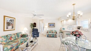 A living room with a sofa, armchair, and a glass coffee table. There is a dining area with a table and chairs. - Closest Shorehaven Unit to Cherry Grove Beach • 4-Min Walk • Sleeps 6 (North Myrtle Beach)