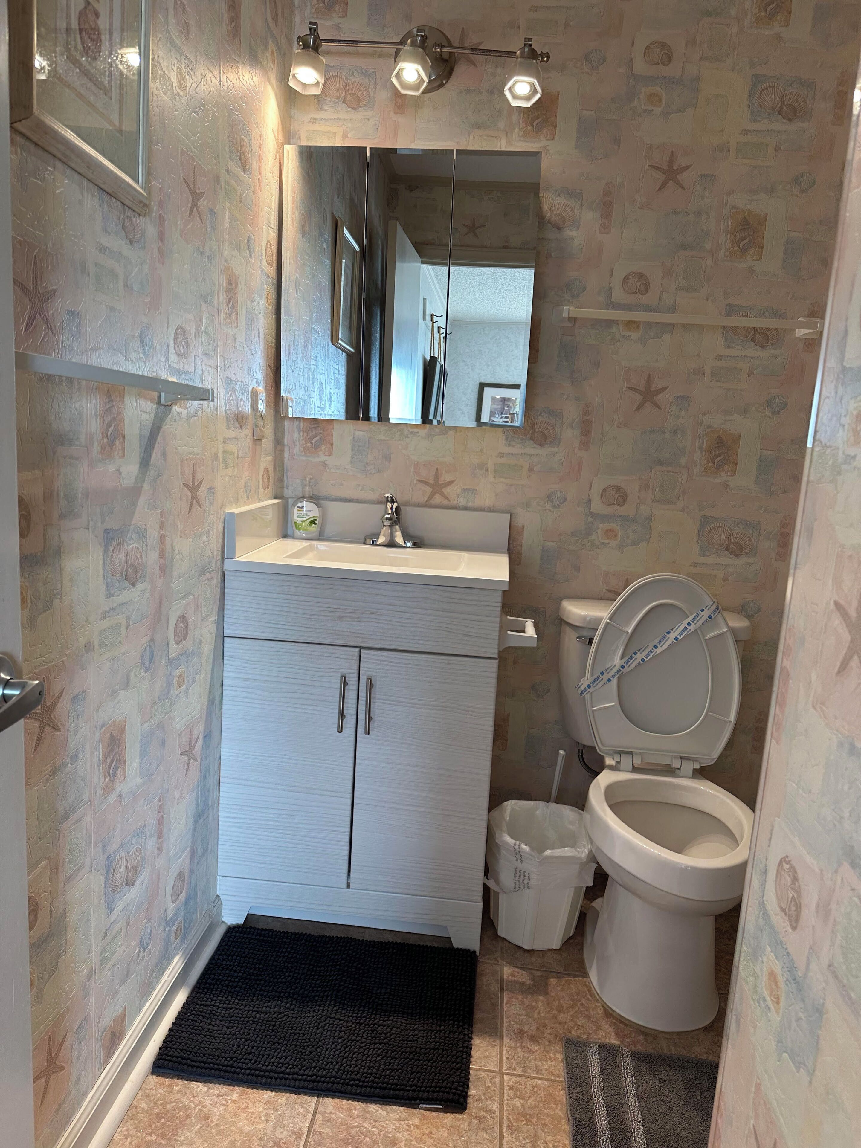 A bathroom with a tiled floor, a white sink with a faucet, a toilet, a mirror above the sink, and a starfish-patterned wall.