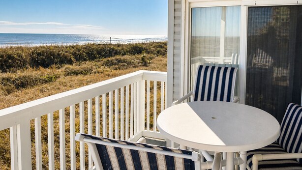 A balcony with a view of the ocean, a white table, and striped chairs. - Corner Oceanfront 2BR – Elevated Balcony Views - Cherry Grove - Beachmaster 107 (North Myrtle Beach)