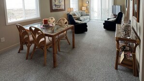 A spacious living room with a dining area, a ceiling fan, and large windows. - Corner Oceanfront 2BR – Elevated Balcony Views - Cherry Grove - Beachmaster 107 (North Myrtle Beach)