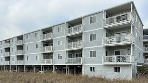 A multi-story residential building with balconies, a flag, and a beach view. - Corner Oceanfront 2BR – Elevated Balcony Views - Cherry Grove - Beachmaster 107 (North Myrtle Beach)