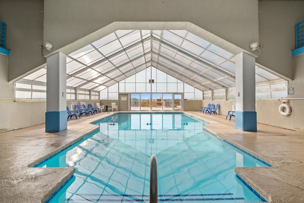 An indoor swimming pool with a high ceiling and skylights, surrounded by blue chairs and a lifebuoy on the wall.