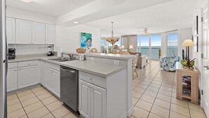 Une cuisine spacieuse avec des meubles blancs, un grand îlot central et une vue sur le salon.