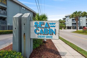 A sign for Sea Cabin in Cherry Grove, featuring a wooden structure with a clear view of the surrounding area including a road and buildings.