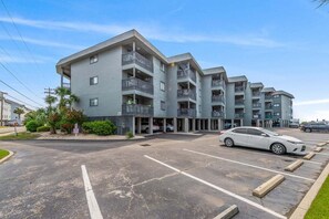 A multi-story residential building with balconies, a parking lot, and a clear sky. - Ocean View 2BR • First-Floor • Cherry Grove • Sea Cabin 125-B (North Myrtle Beach)