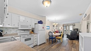 Una cocina con armarios blancos, un microondas, un refrigerador y un comedor con mesa y sillas.