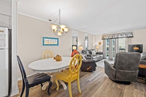 A dining area with a white table and chairs, a sofa, and a recliner in a living room. - Ocean View 2BR • First-Floor • Cherry Grove • Sea Cabin 125-B (North Myrtle Beach)