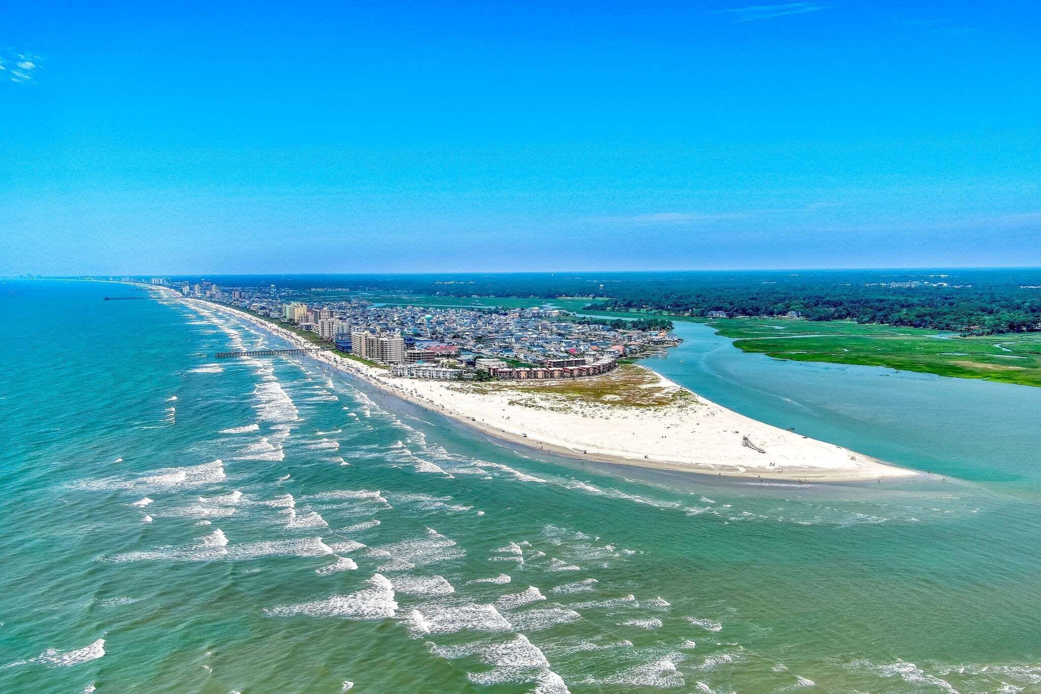 An aerial view of a coastal city with a long beachfront, a pier, and dense urban development.