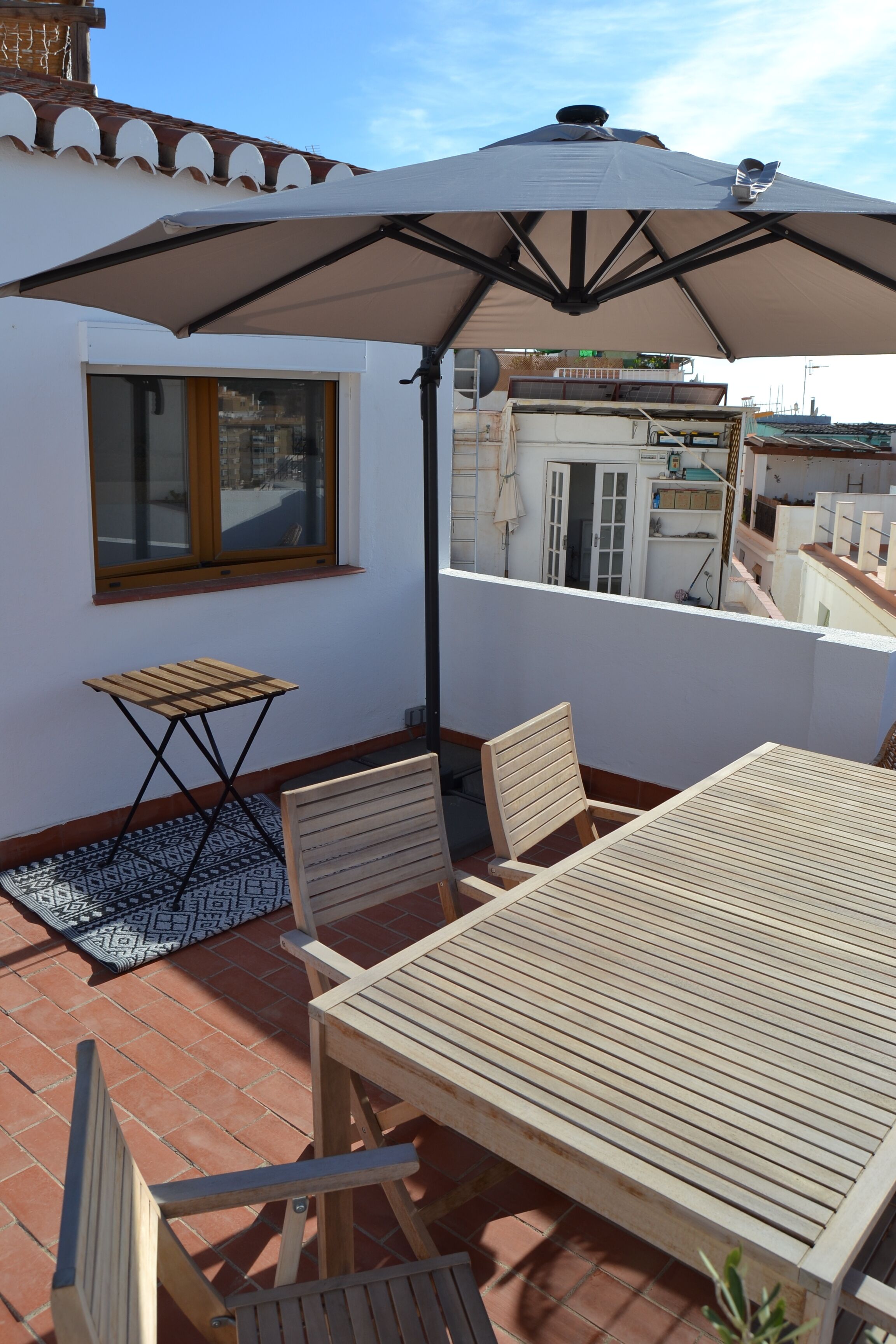 An outdoor patio with a table and chairs, a small folding table, and a large umbrella providing shade.