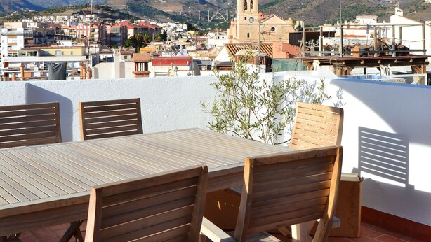 A terrace with a table and chairs, a large umbrella, and a view of a town with a church and mountains in the background. - Typical Andalusian house in the heart of the historic center (Almuñécar)
