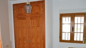 A bedroom with a large wooden wardrobe, a bed with a green and yellow pillow, a small bedside table with a lamp, and a window with bars. - Typical Andalusian house in the heart of the historic center (Almuñécar)