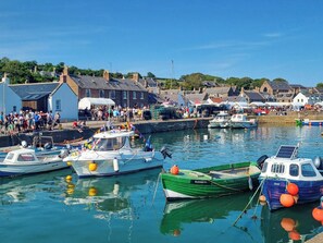 A harbor with boats docked, a crowd of people, and buildings in the background. - 2 bedroom accommodation in Johnshaven (Johnshaven)