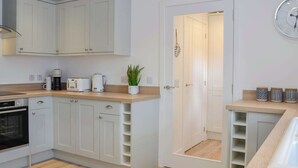 Una cocina moderna con armarios blancos, horno integrado y una cafetera en la encimera.