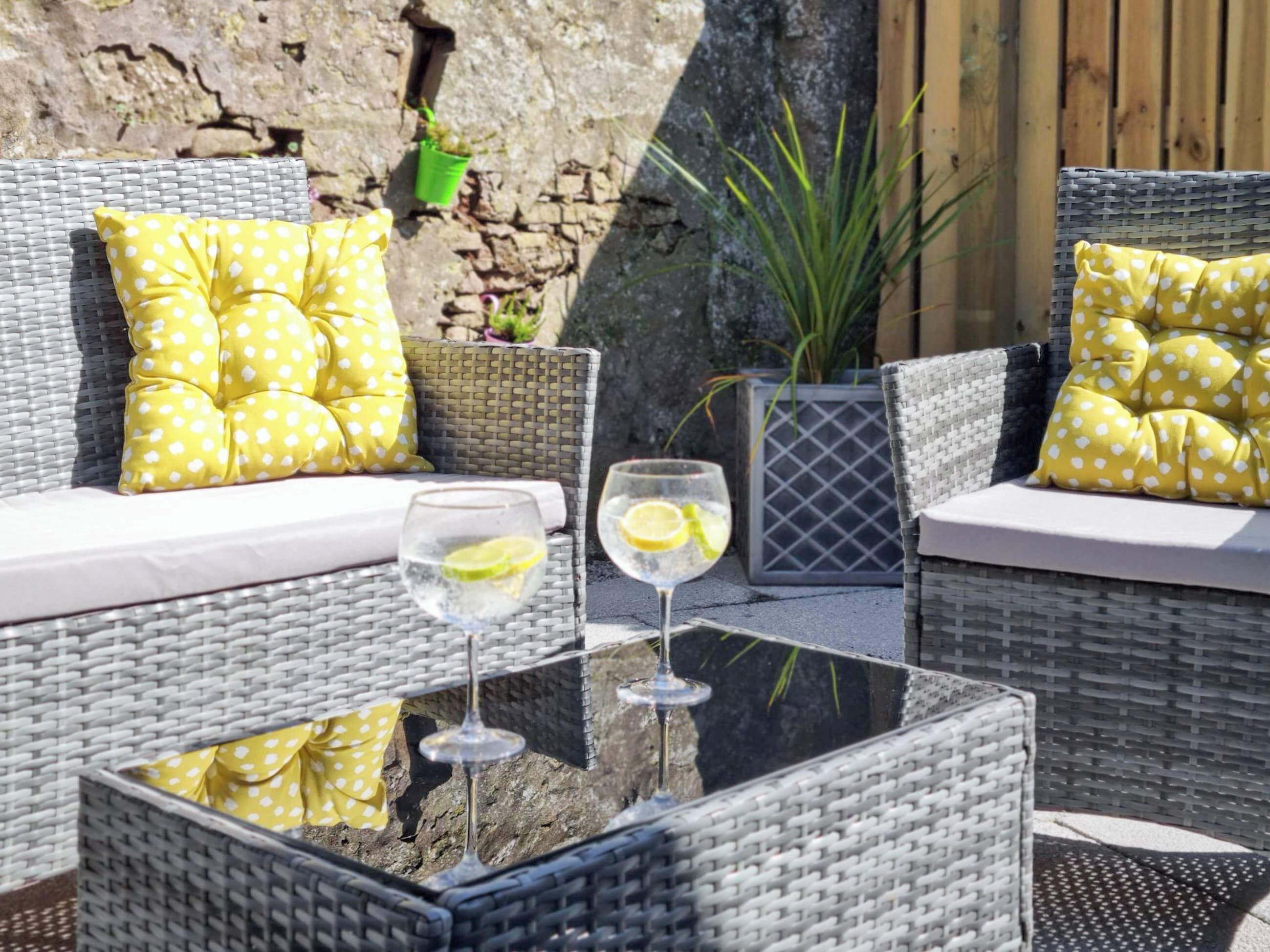 A wicker outdoor seating area with cushions, a glass table, and a potted plant.