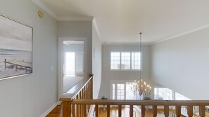 A spacious room with a wooden staircase, large windows, and a chandelier. - Ocean Drive Oceanfront 6BR • All En-Suite • Private Pool • Sleeps 20 • Ibis (North Myrtle Beach)