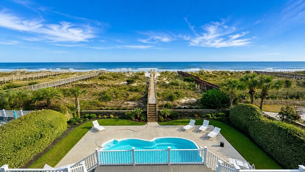 A pool area with a view of the ocean, a wooden deck, and a pathway leading to the beach.