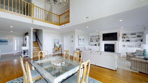 A spacious living area with a glass-top dining table, wooden chairs, a fireplace, and a staircase leading to an upper level.
