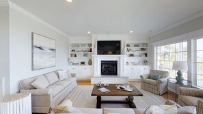A spacious living room with a fireplace, white furniture, and large windows. - Ocean Drive Oceanfront 6BR • All En-Suite • Private Pool • Sleeps 20 • Ibis (North Myrtle Beach)