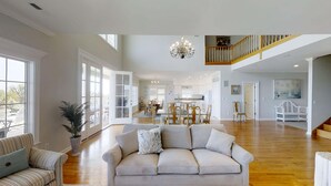 A spacious living area with a large sofa, dining table, and chairs, a staircase, and a kitchen in the background.