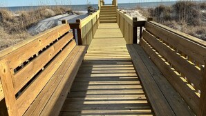 A wooden boardwalk leading to a beach with benches on either side.