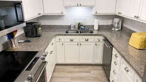 Una cocina con armarios blancos, una estufa negra, una cafetera y un paño amarillo sobre la encimera.