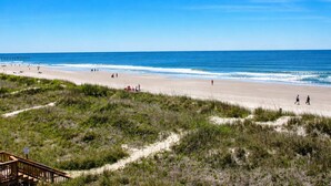 Una playa con un paseo de madera que lleva a una estructura, cielo despejado y el océano.