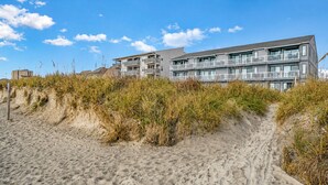 Un hotel frente a la playa con varios balcones y un camino de arena que lleva al edificio.