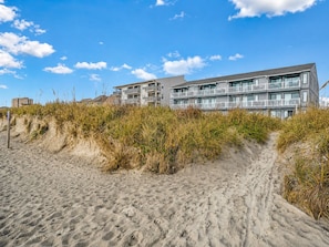 Un hôtel situé en bord de mer, doté de nombreux balcons et d’un sentier sablonneux menant au bâtiment.