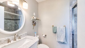 Un baño con lavamanos de mármol, un espejo redondo, un perchero para toallas y una ducha.
