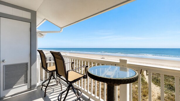 Un balcón con dos sillas y una mesa, con vista a la playa.