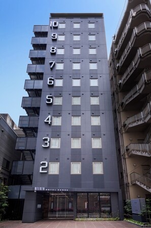 Un hôtel moderne, avec un bâtiment à dix étages numérotés de 1 à 10, une entrée en verre et une cour intérieure agrémentée de plantes.