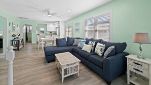 A spacious living area with a large sectional sofa, a small coffee table, and a dining area in the background. - Oceanfront 5BR Home • Back Deck on the Beach • Cherry Grove • Momma’s Gift (North Myrtle Beach)