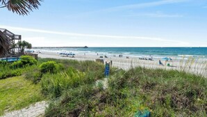 A beach with a wooden structure, a pier in the distance, and a signboard. - Oceanfront 5BR Home • Back Deck on the Beach • Cherry Grove • Momma’s Gift (North Myrtle Beach)