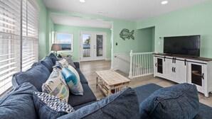 A living room with a sofa, a coffee table, a TV on a cabinet, and a fish wall decoration. - Oceanfront 5BR Home • Back Deck on the Beach • Cherry Grove • Momma’s Gift (North Myrtle Beach)
