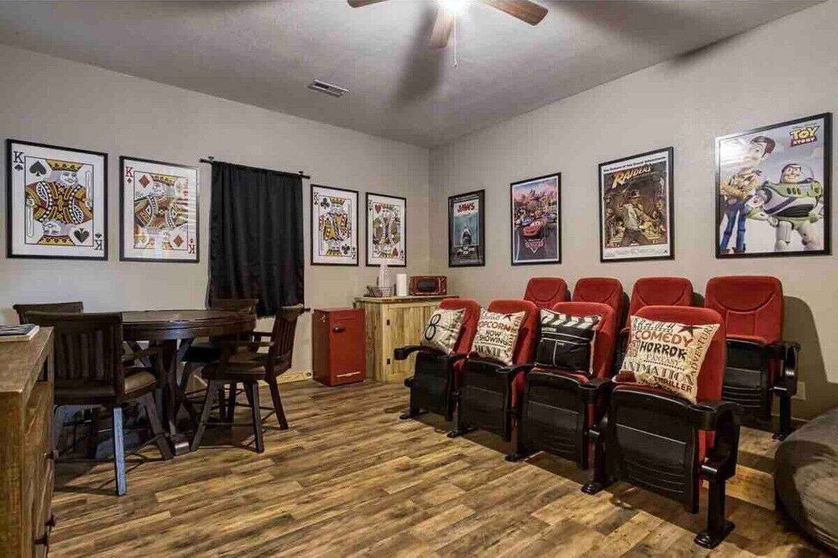 A room with a wooden floor, a dining table with chairs, a red cabinet, and a row of red and black chairs with movie-themed cushions.