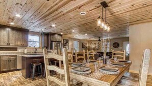 Un intérieur rustique en bois, avec une grande table à manger dressée pour quatre personnes, entourée de chaises en bois.