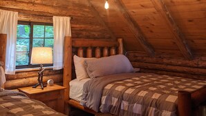 Una habitación tipo cabaña acogedora con una cama en altillo, una mesita de noche con lámpara y una ventana con cortinas.