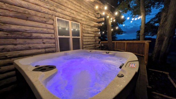 Un jacuzzi frente a una cabaña de troncos con luces colgantes.