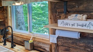 Una cocina rústica con encimera de madera, una ventana con vistas a zonas verdes, una lámpara colgante y un letrero en la pared.