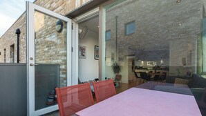Eine offene Terrasse mit Tisch und Stühlen, einer Schiebetür und einer Backsteinmauer.