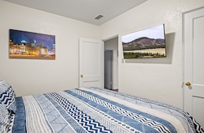 A bedroom with a bed, a cityscape painting, a landscape painting, and a door.