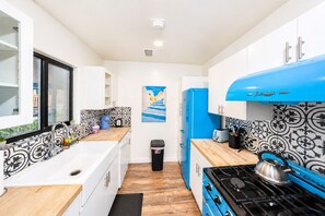 A compact kitchen with white cabinets, a blue refrigerator, and a black stove. - Route 66 Bodacious Bungalow w/AC, Fully Fenced Yard, W/D, 4 Smart TVs, Fast WiFi (Williams)