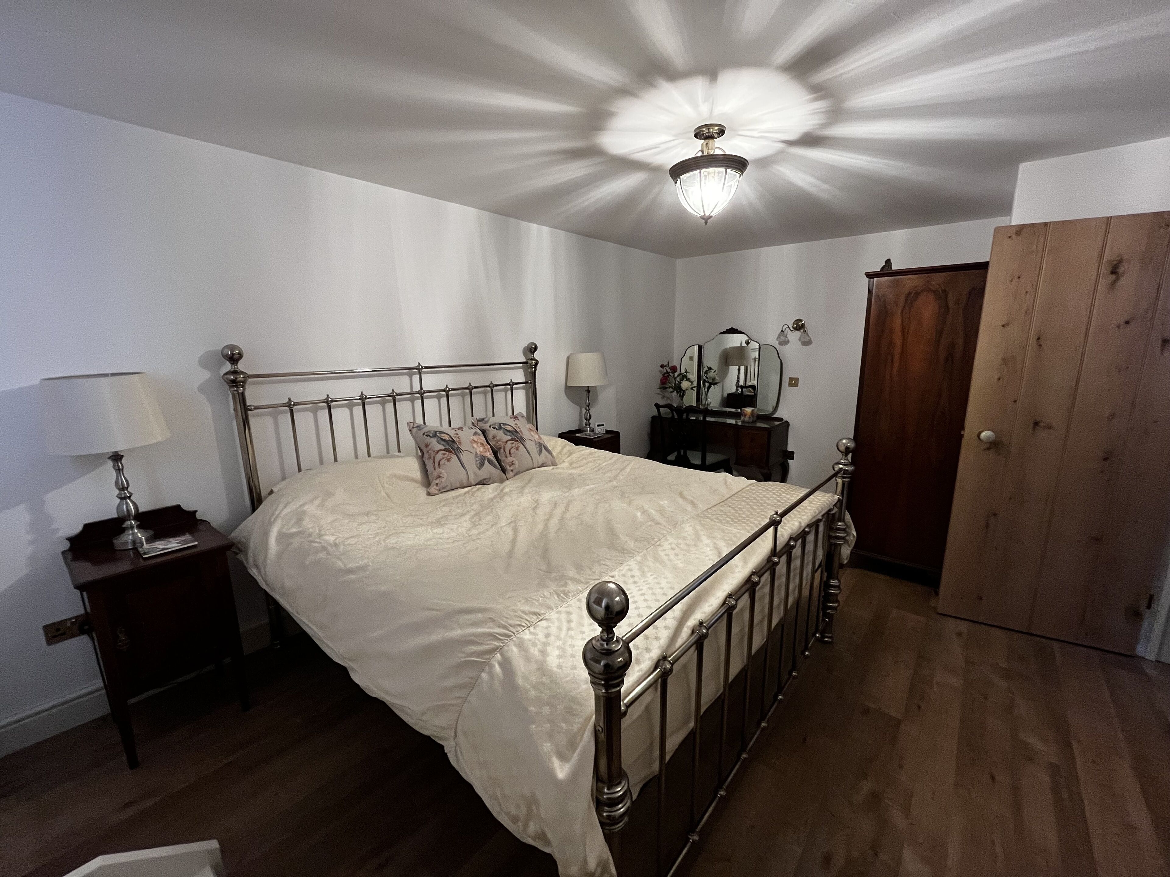 Une chambre à coucher avec un lit à ossature métallique, deux tables de chevet avec des lampes, une armoire en bois et un luminaire fixé au plafond.
